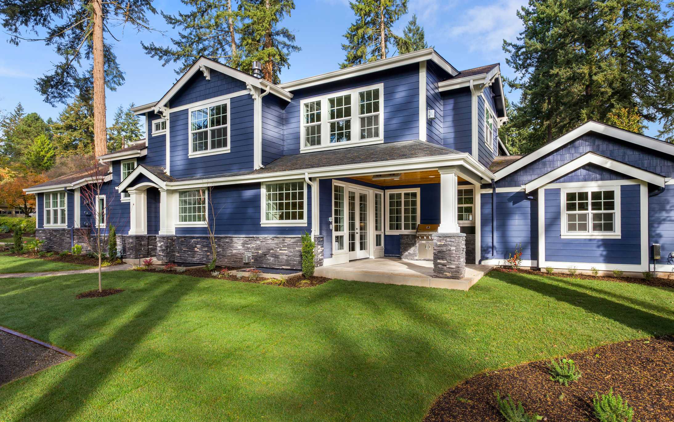 A home with manicured lawn, and backdrop of trees and blue sky